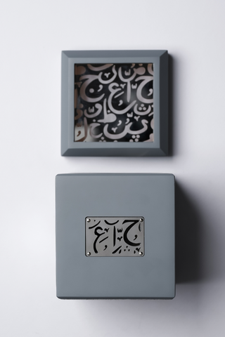 A gray mubkhar (Arabic incense burner) with Arabic calligraphy decoration, viewed from the top and front, showing the burner's lid and the incense compartment by Atyab Al Marshoud.